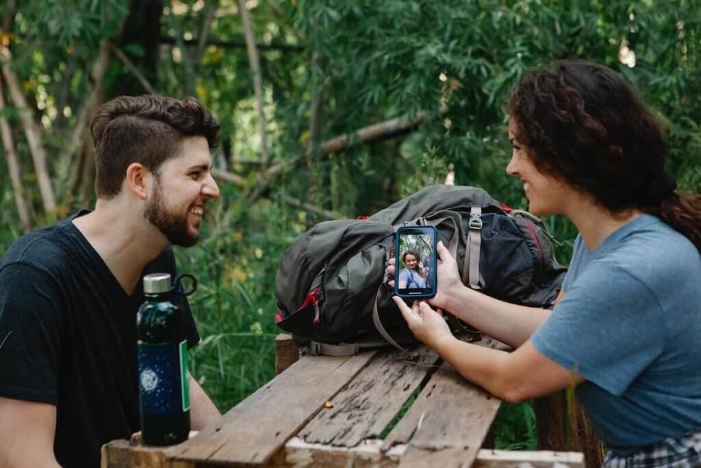 Happy young woman sharing smartphone with friend in forest